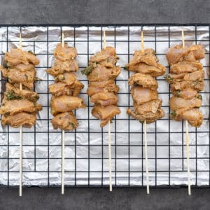 A baking tray with chicken skewers and ready for cooking.