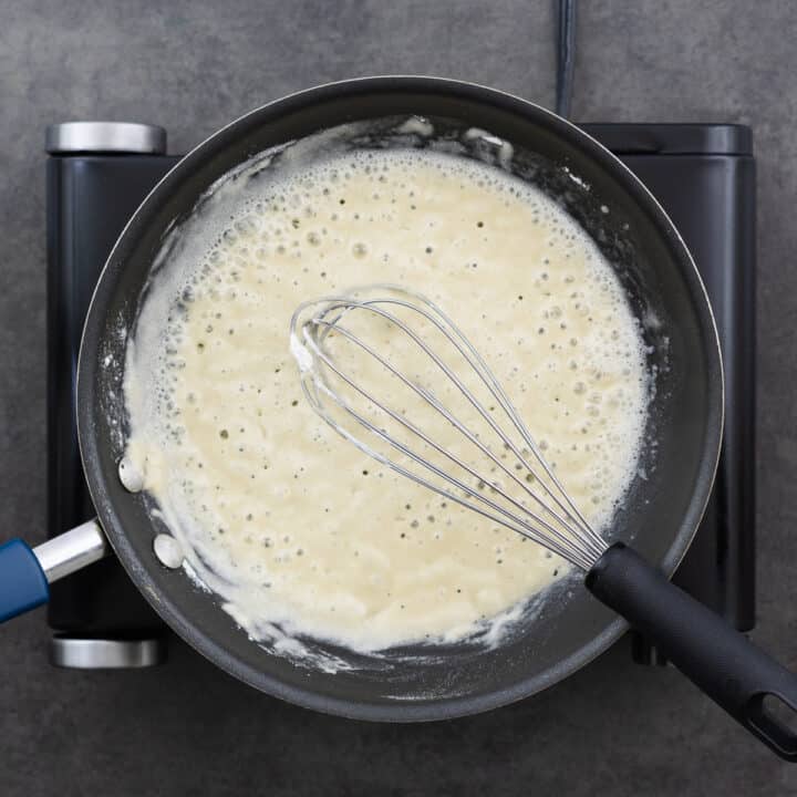 A pan with roux mixed using a whisk.