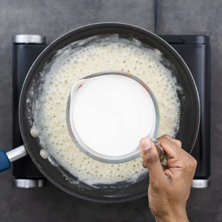 Adding milk to the prepared roux mixture in a pan.