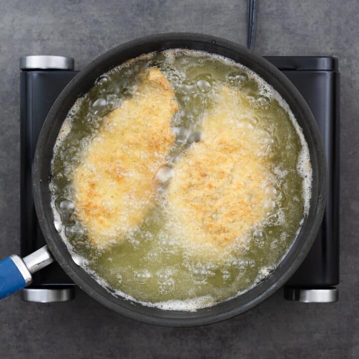 A pan with flour-coated chicken breast frying in hot oil.