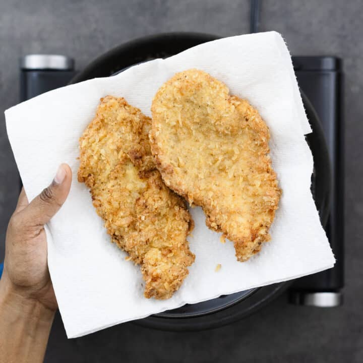 Nicely fried chicken breast removed from oil and displayed on a plate lined with a paper towel.