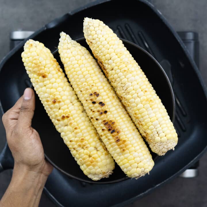 A nicely grilled corn cob on a black plate, showcasing the golden, charred kernels.