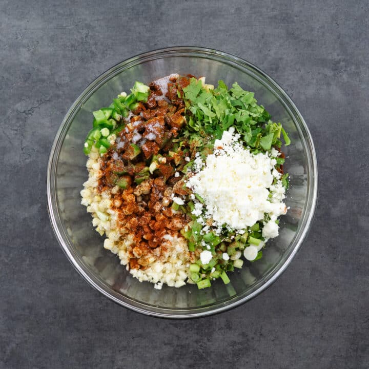 Corn salad ingredients placed in a wide bowl, featuring colorful seasonings, fresh herbs, and cheese.