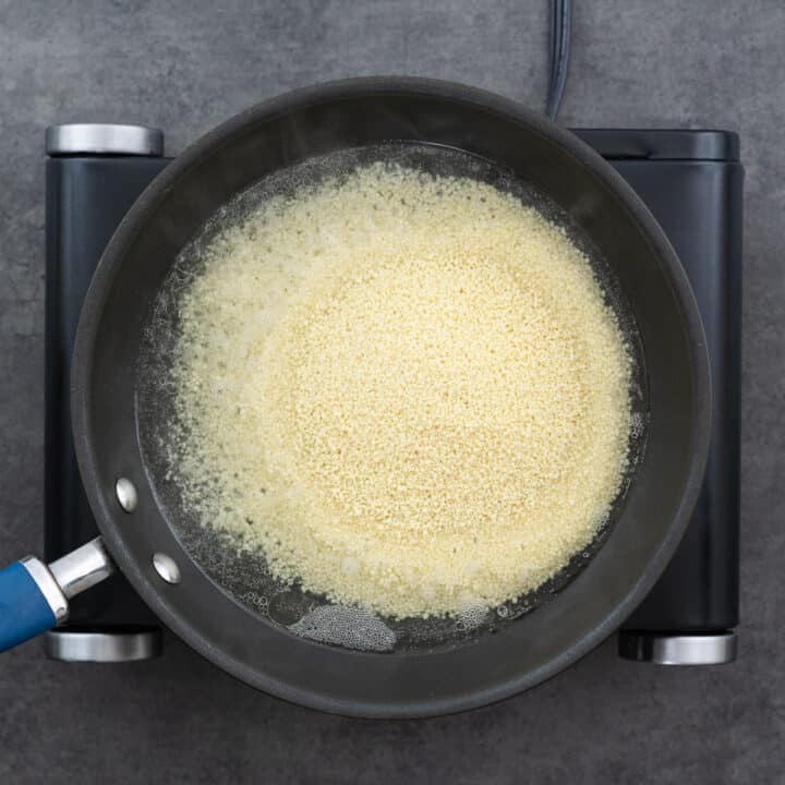 A saucepan with boiling water and couscous added, starting the cooking process.