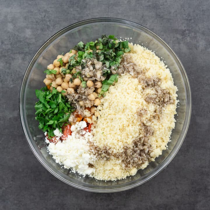 A large bowl with a mix of couscous, chopped veggies, garbanzo beans, and the dressing, ready to be tossed.