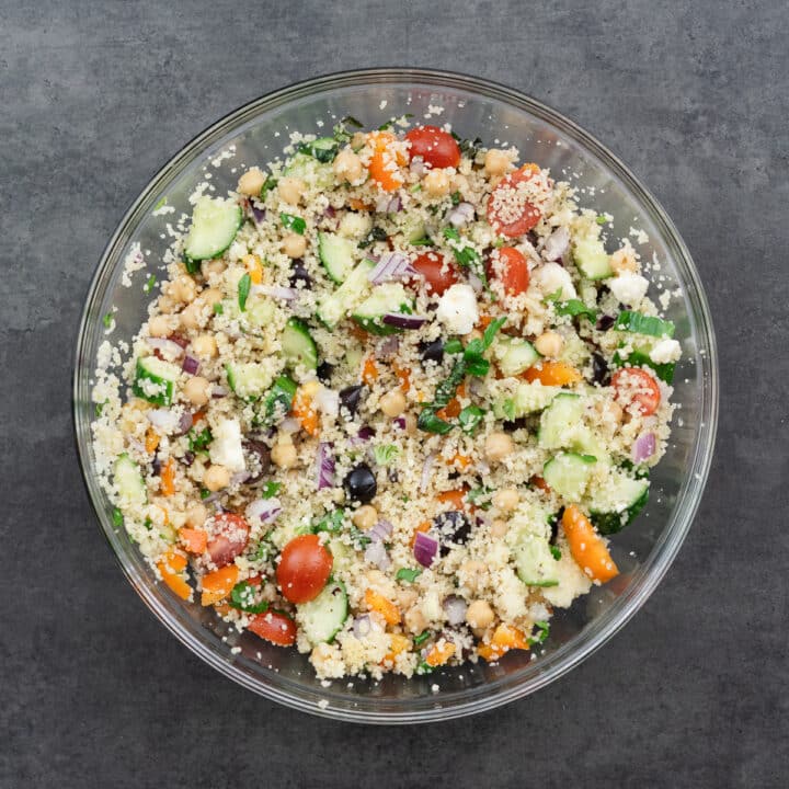 A bowl of couscous salad, thoroughly mixed with the dressing, showing a well-combined, colorful dish.