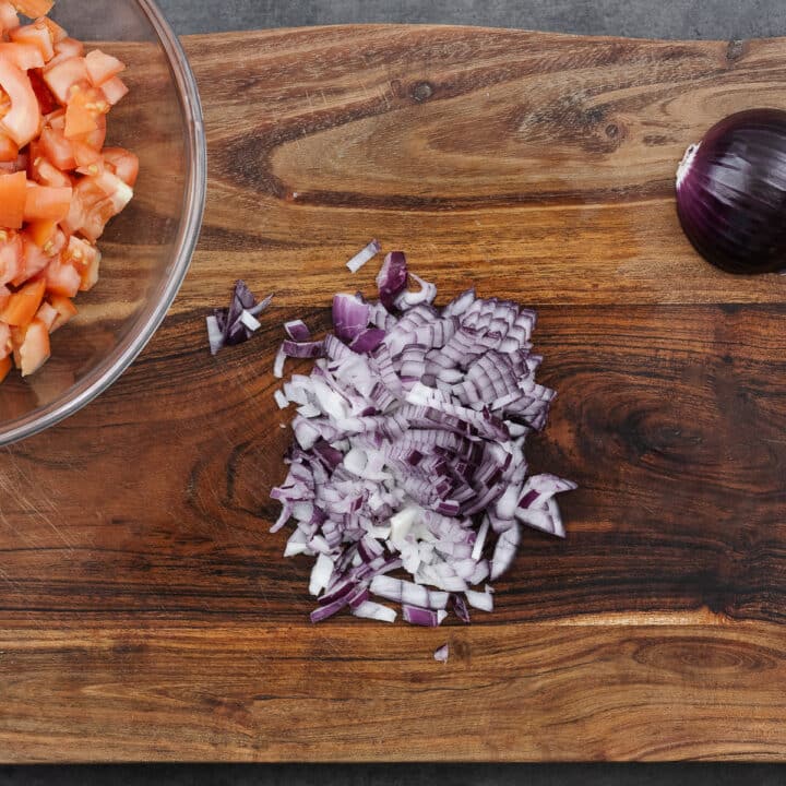 Finely chopped red onions spread out on a wooden cutting board.