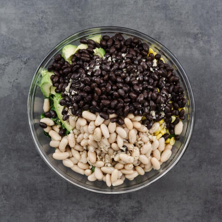 A mixing bowl filled with Cowboy Caviar ingredients, all coated in a tangy vinaigrette dressing.