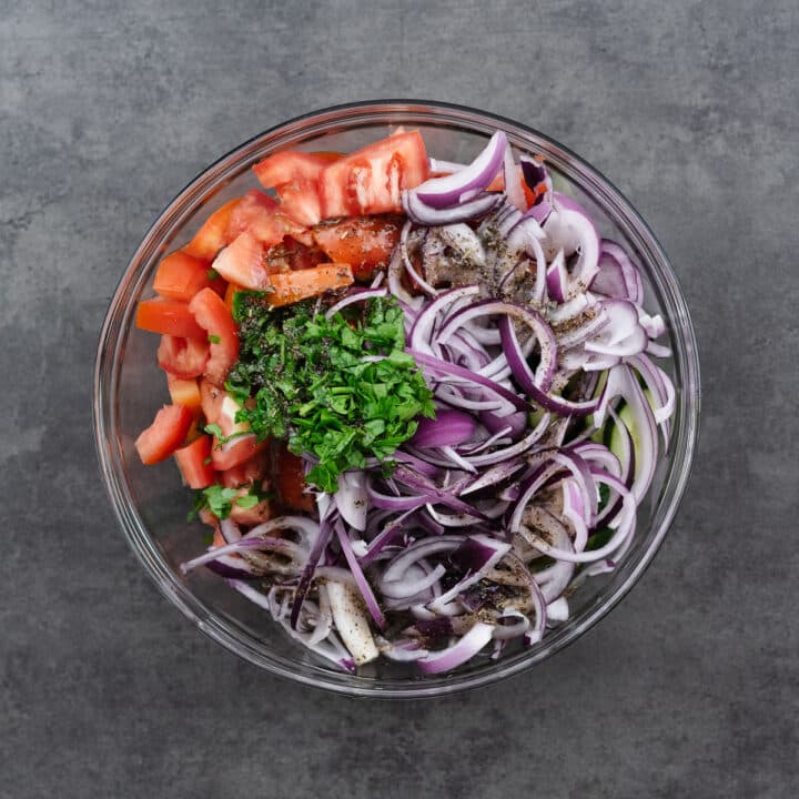 A large bowl with chopped cucumbers, tomatoes, and onions, ready to be mixed with vinaigrette.