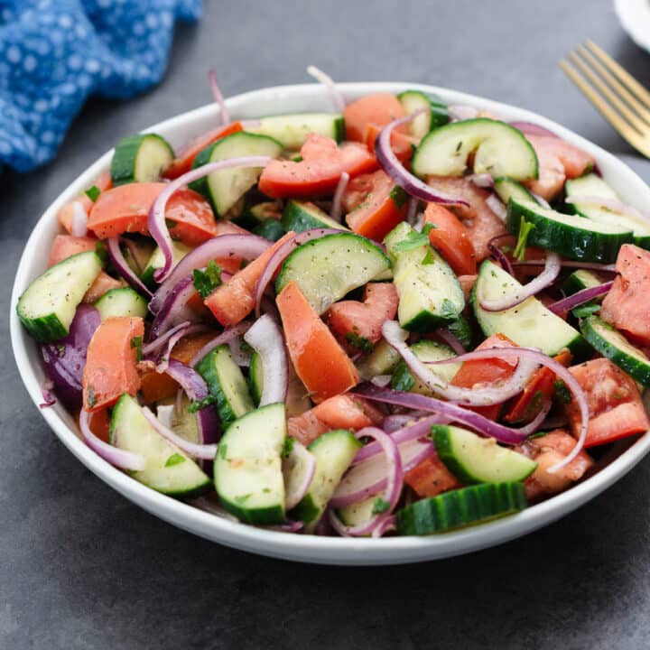 Cucumber tomato salad served in a white bowl, and ready to enjoy.