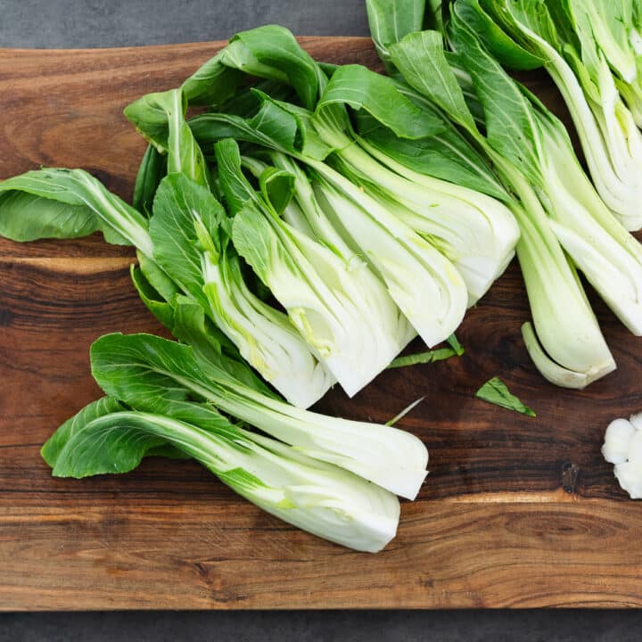 Freshly quartered baby bok choy on a wooden board, ready for cooking.