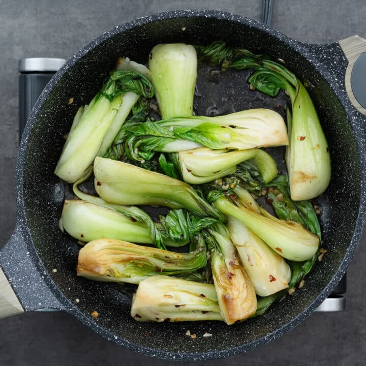 Bok choy being sautéed in a pan with seasonings, absorbing all the flavors.