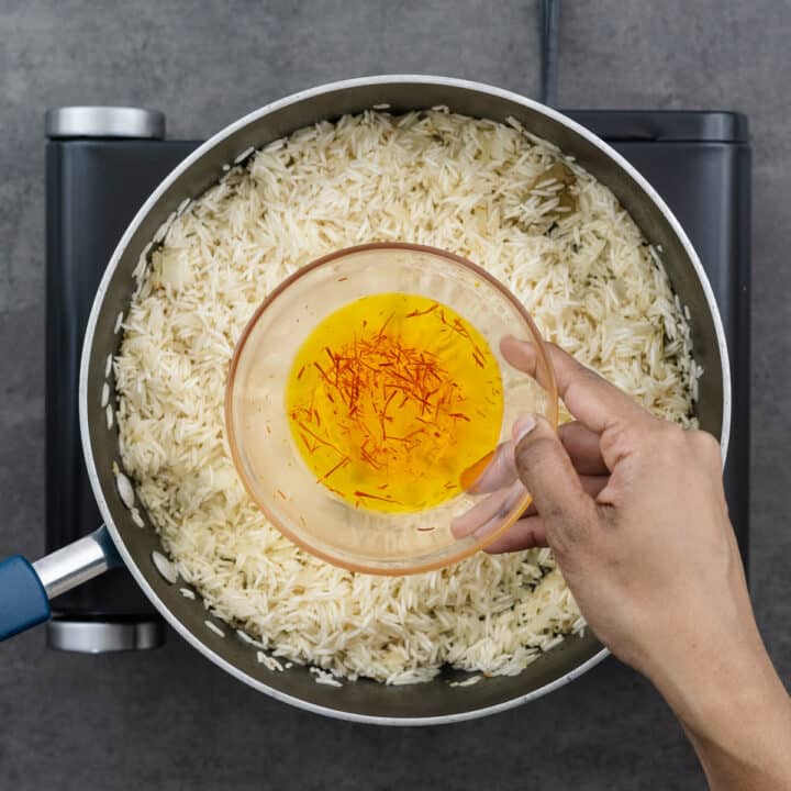 Adding bloomed saffron water to the rice mixture in the pan.