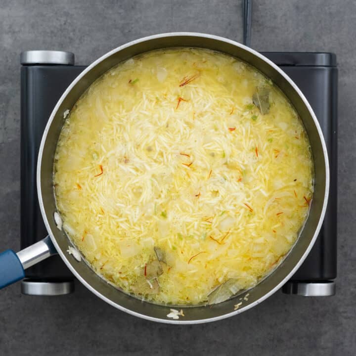 Saffron rice mixture boiling in broth on the stove.