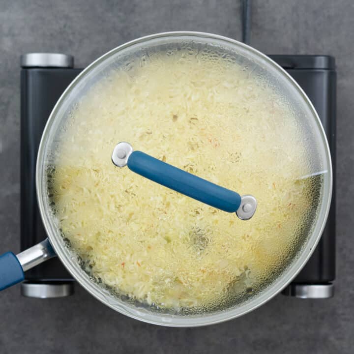 Saffron rice mixture cooking with the lid covered on the stove.