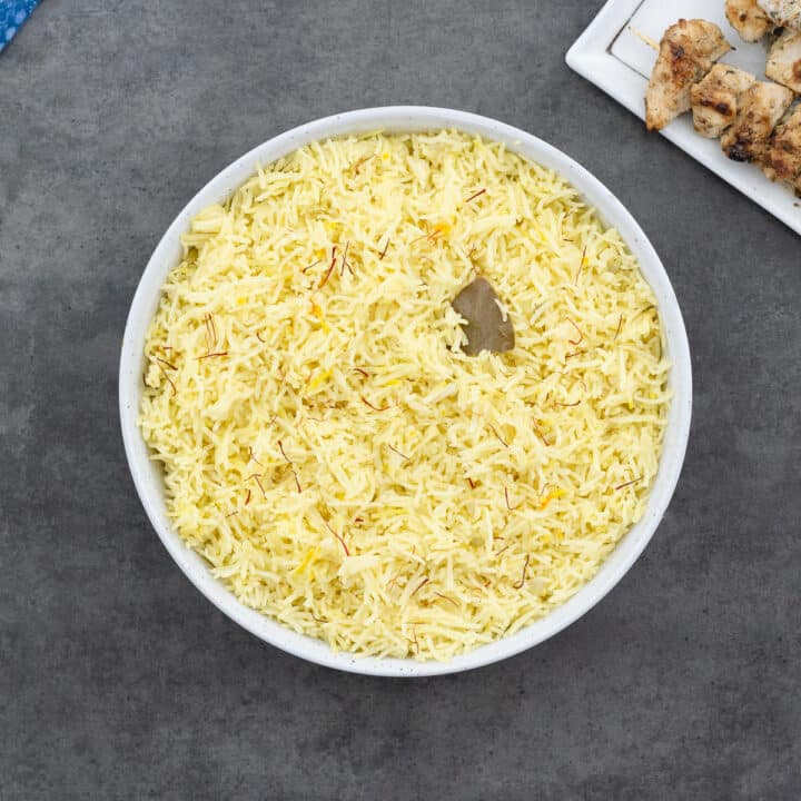 Saffron rice served in a white bowl alongside chicken souvlaki.