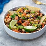 Homemade Texas Cowboy Caviar served in a white bowl on a white table, accompanied by a blue towel, and a golden fork nearby.