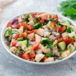 Fresh homemade shrimp ceviche in a white bowl on a white table, with cilantro nearby.