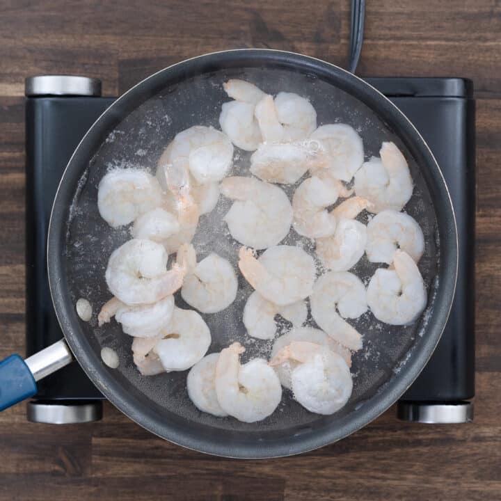 A pan with shrimp cooking in boiling water, turning pink as they cook.