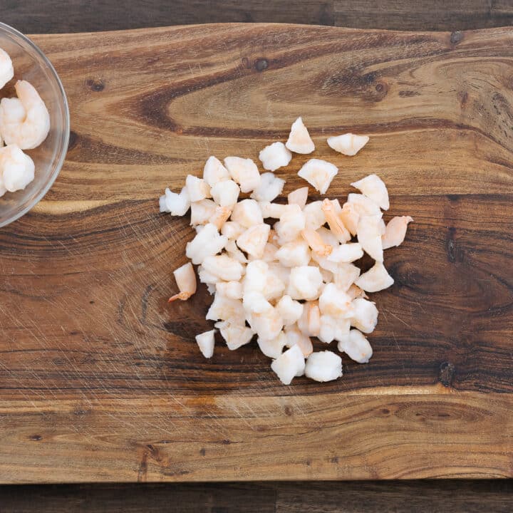 A wooden cutting board showing freshly chopped shrimp, cut into bite-sized pieces.