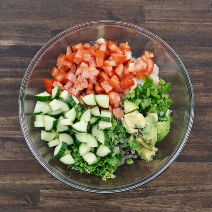 A bowl filled with chopped shrimp, fresh vegetables, herbs, and citrus juices like lime and orange, ready to mix.