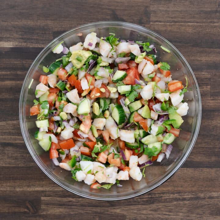 A colorful bowl of shrimp ceviche with fresh veggies and herbs, all mixed together.