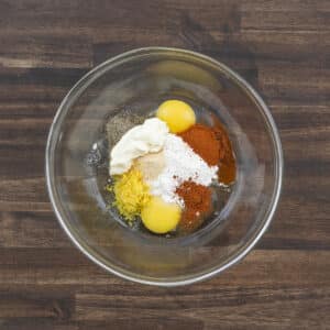 A bowl filled with eggs, mayonnaise, seasonings, and flour, ready to be mixed.
