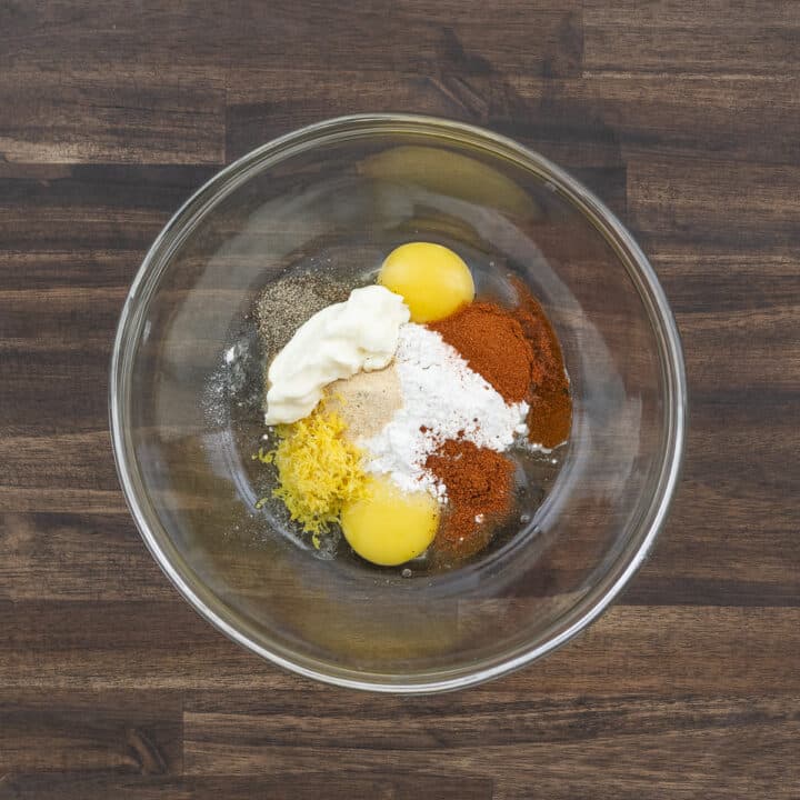 A bowl filled with eggs, mayonnaise, seasonings, and flour, ready to be mixed.