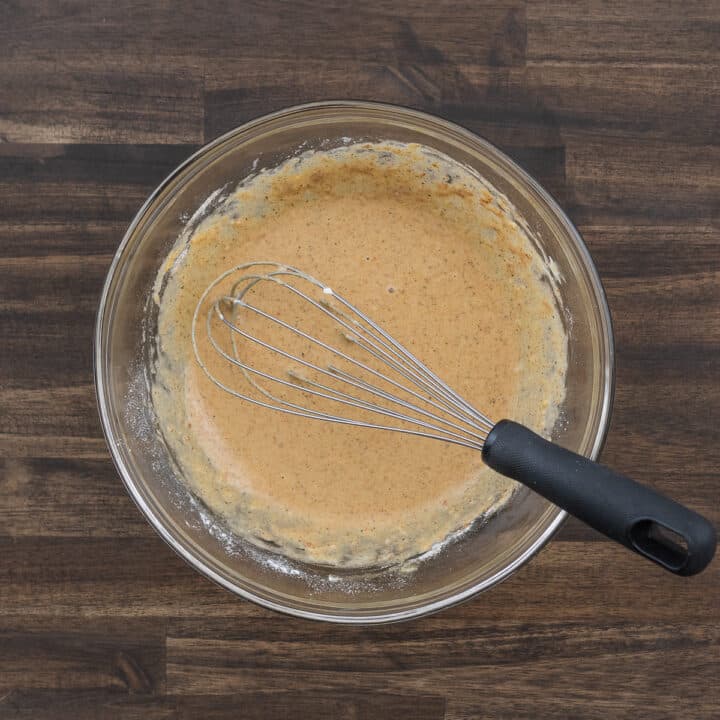 A bowl containing the marinating mixture alongside a whisk.