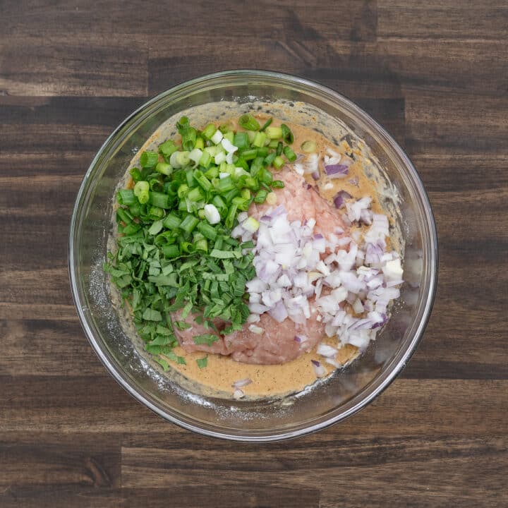 A bowl of marinating mixture with ground chicken, aromatics, and herbs.