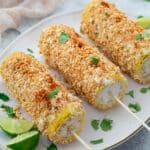 Elote, Mexican street corn, served with lime on an oval plate on a white table. A towel placed nearby.