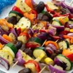 Grilled vegetable skewers on a white plate set on a white table.