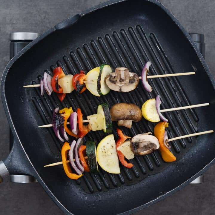 A grill pan filled with nicely grilled vegetable skewers, showing char marks and vibrant colors.