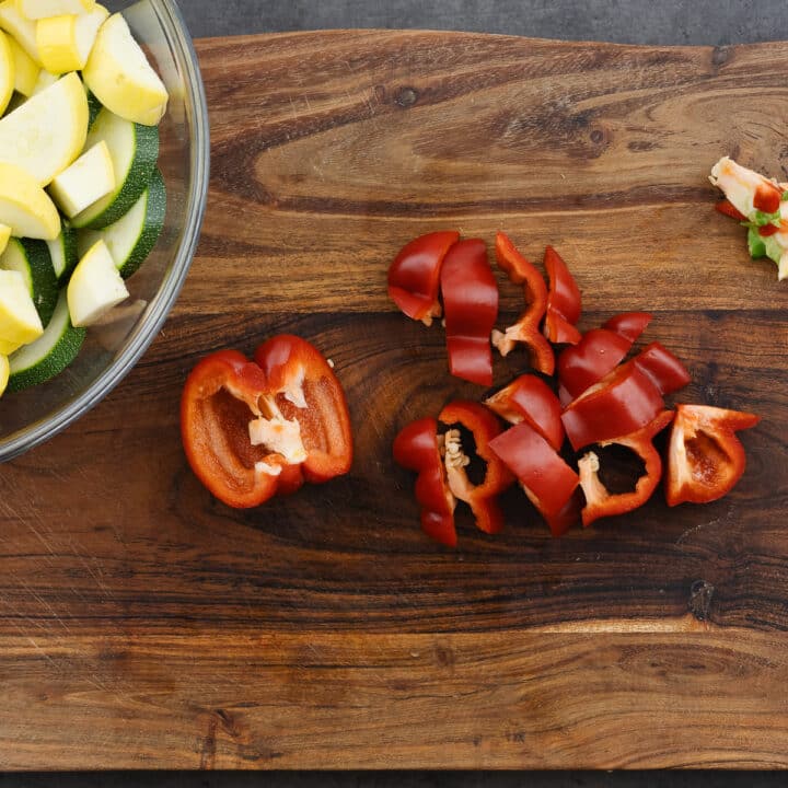 A wooden board displaying diced red bell peppers, ready for grilling.