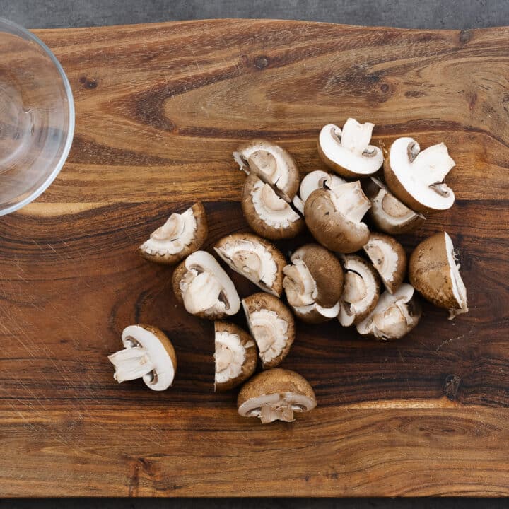 A wooden board featuring halved mushrooms, prepared for skewering.