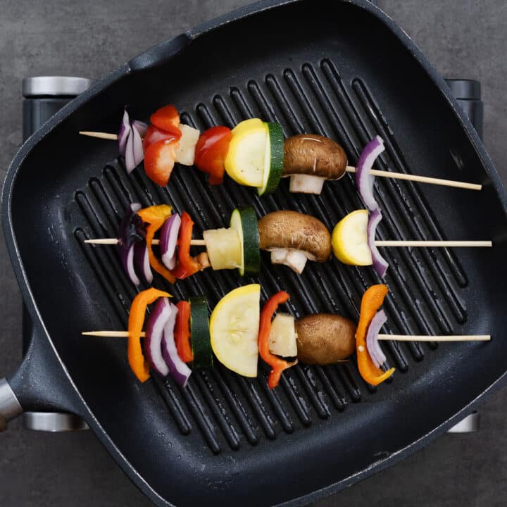 A grill pan with vegetable skewers placed on it, ready to be cooked.