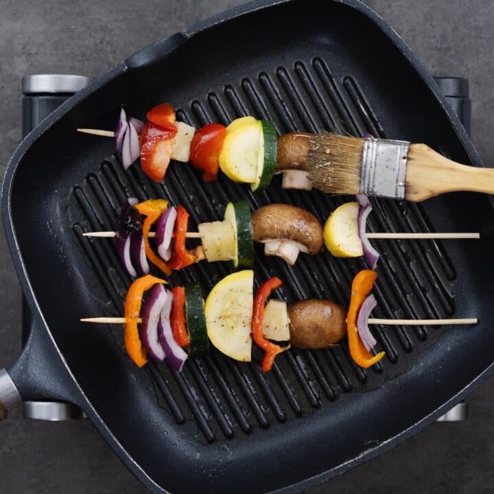 A grill pan with vegetable skewers that have been brushed with marinade.