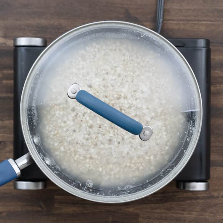 A pan with barley cooking, covered with a lid.