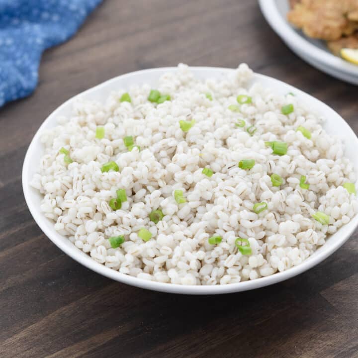 Barley garnished with scallions, served in a white bowl.