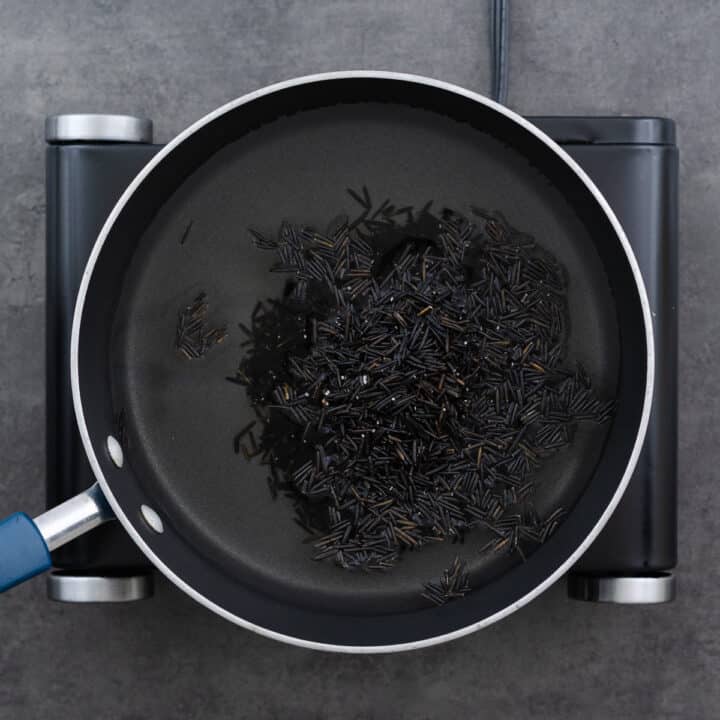 A wide pan filled with water and uncooked wild rice, ready to cook on the stovetop.