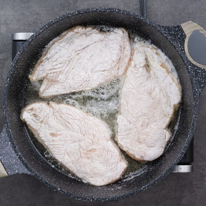 A pan with flour-coated chicken breasts frying in a mixture of oil and butter.