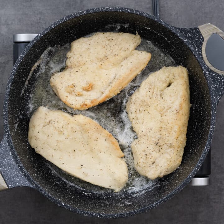 Chicken breasts in a pan, frying to a golden color in oil and butter.