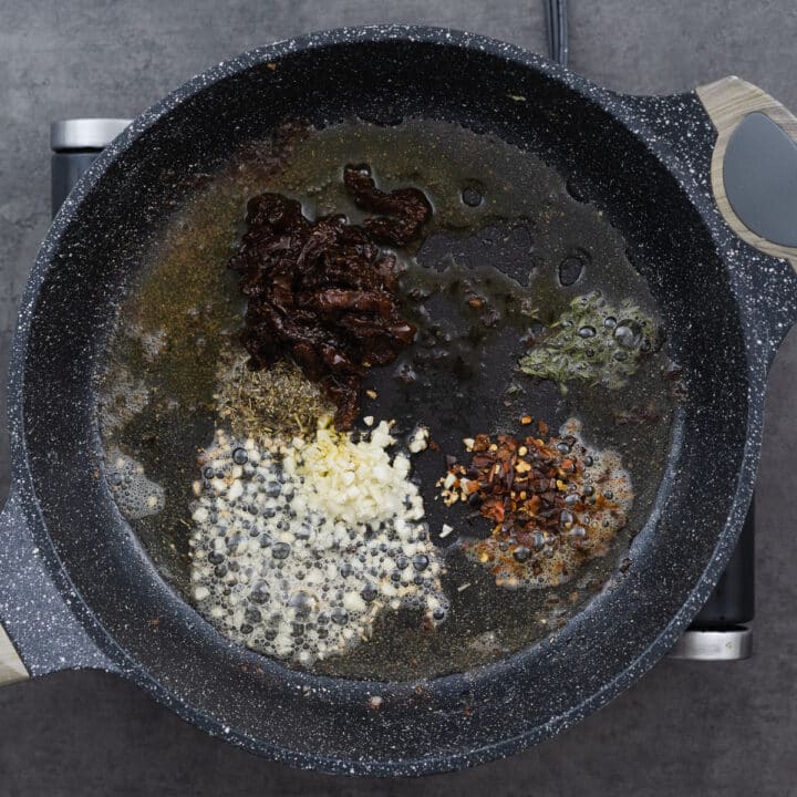 A pan with minced garlic, herbs, and aromatics sizzling in a mixture of oil and butter.