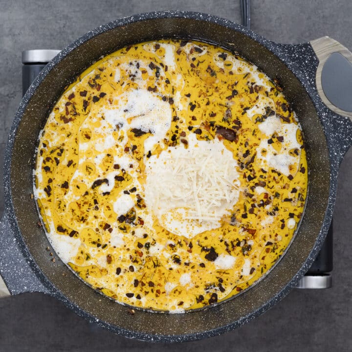 A pan with heavy cream, chicken stock, and Parmesan cheese simmering to form a creamy sauce.