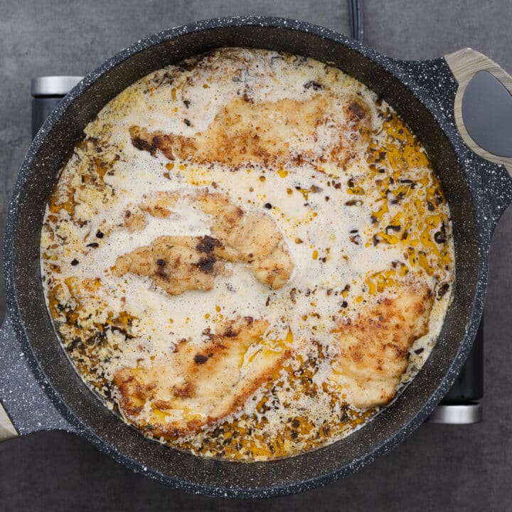 A pan with pan-fried chicken breasts simmering in the creamy sauce.