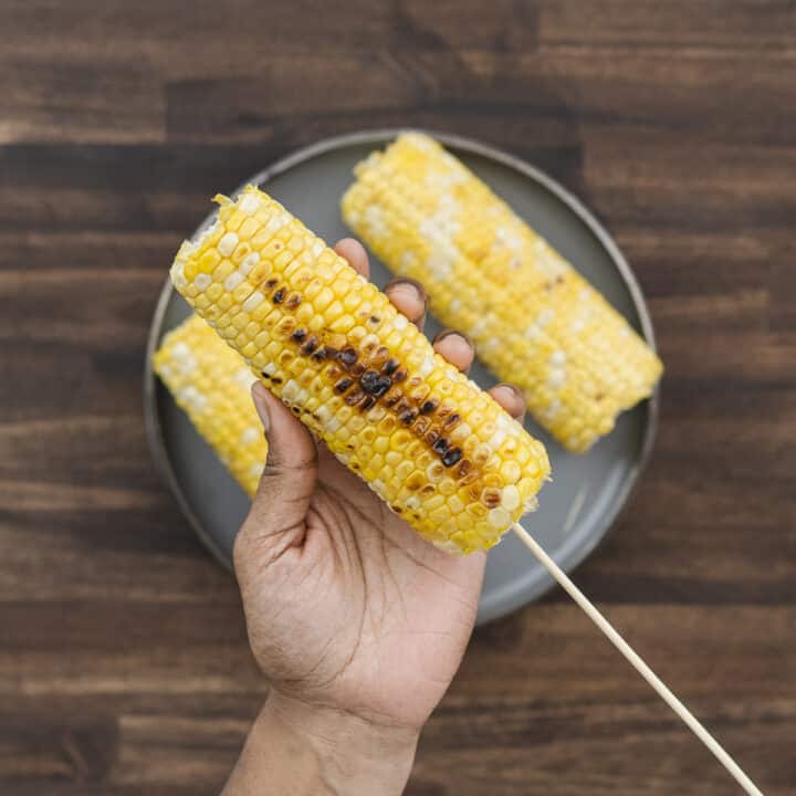 Skewering grilled corn with a wooden stick for easy handling.