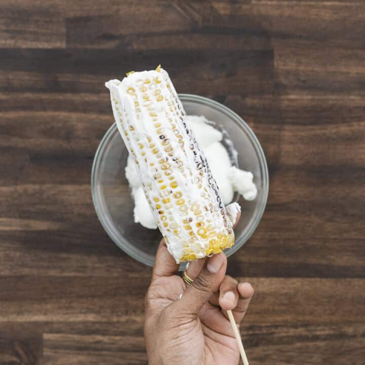 Grilled corn coated with a layer of Mexican crema using a spatula.