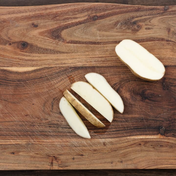 A wooden cutting board displaying freshly cut potato wedges, ready for seasoning.