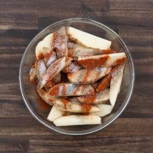 A bowl filled with potato wedges and a blend of spices and seasoning.