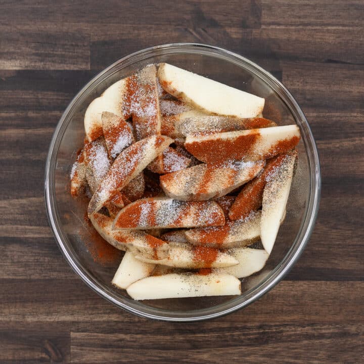 A bowl filled with potato wedges and a blend of spices and seasoning.